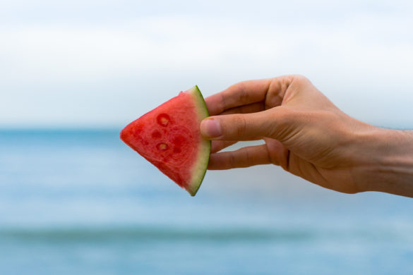 Guy holding watermelon slice on the beach